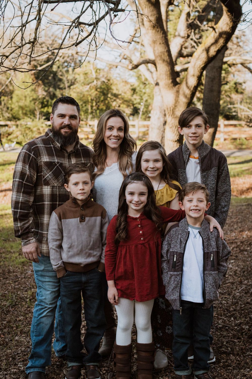 A casual outdoor family portrait taken in an autumn setting with trees in the background.