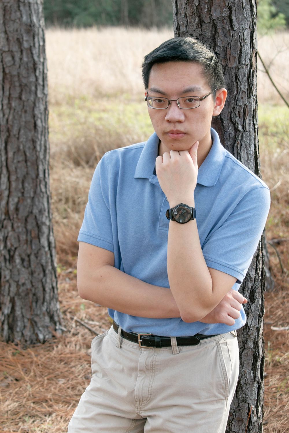A thoughtful portrait of a musician in blue polo leaning against a pine tree.