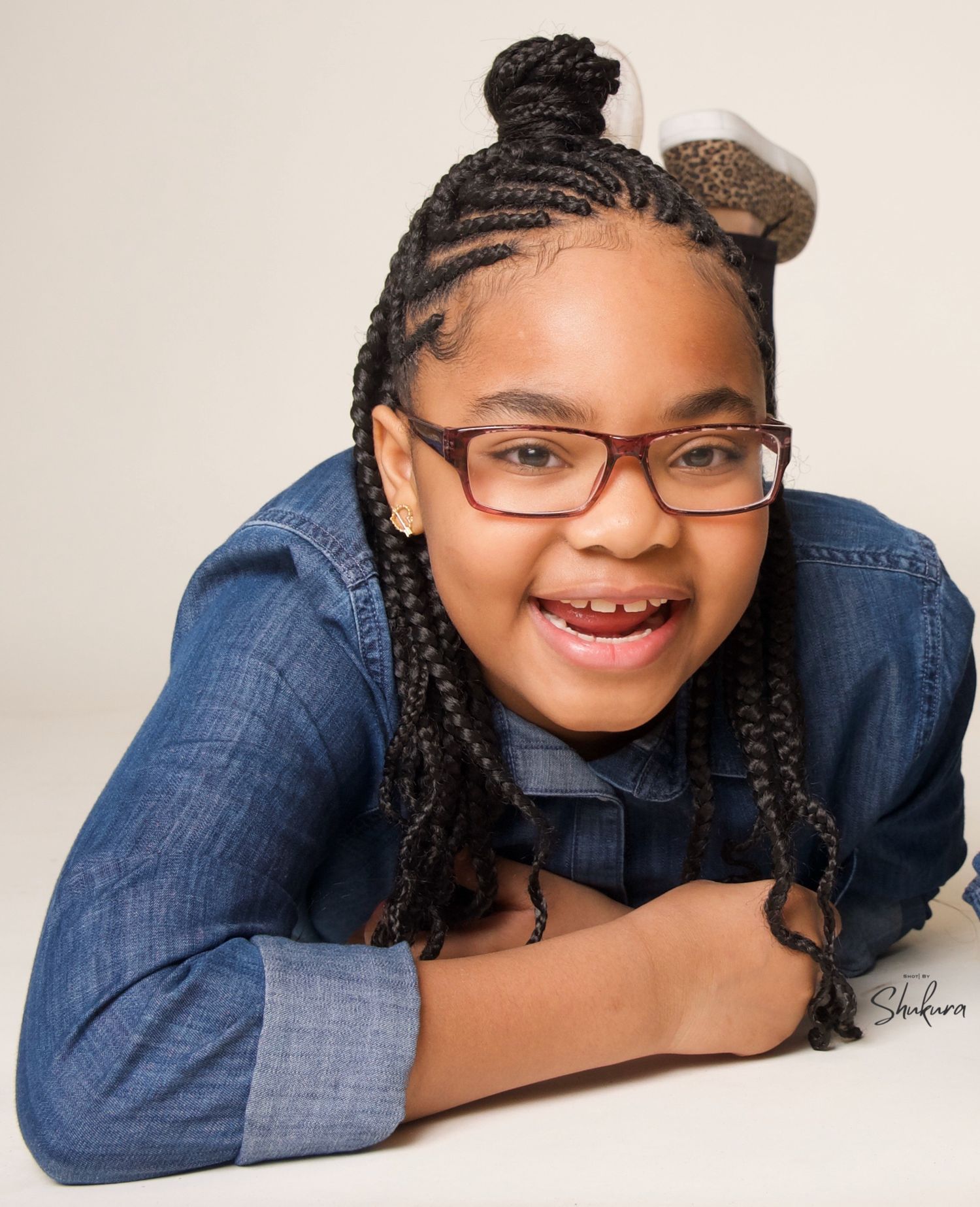 Portrait of person in denim shirt with braided hair and glasses smiling at camera.