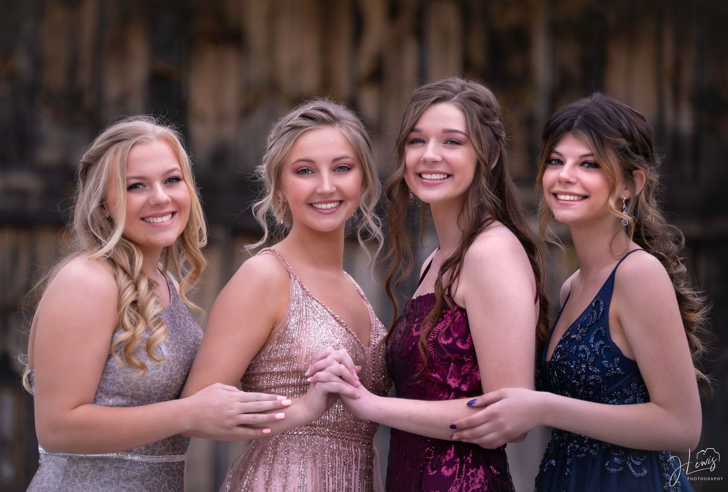 Four friends in formal dresses pose together at a special event with elegant styling.