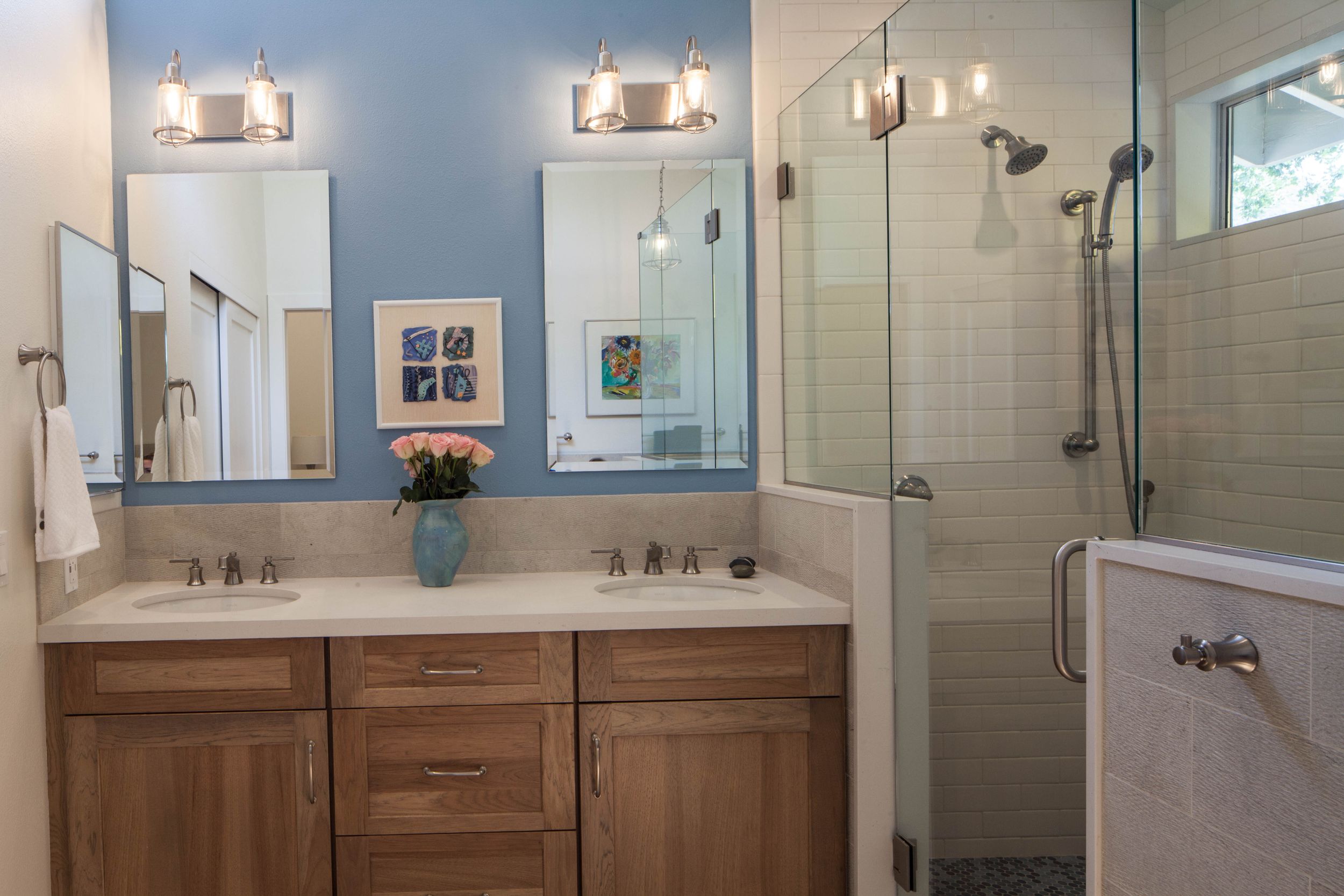 Modern bathroom with dual vanity, blue walls, and glass shower enclosure.