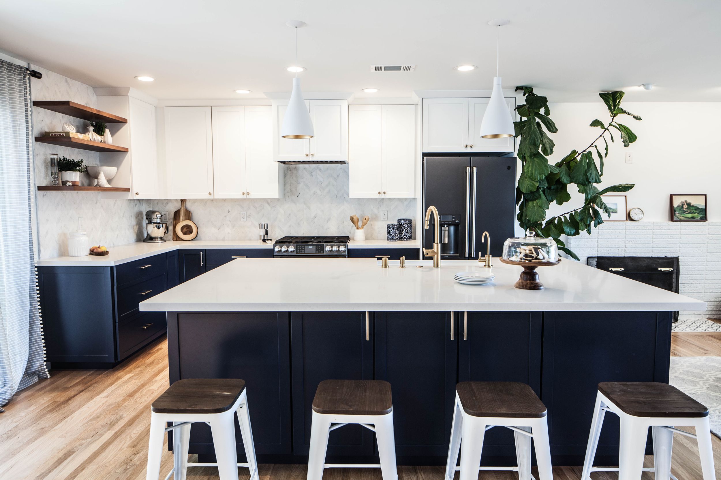 Modern kitchen featuring black lower cabinets, white uppers, and metal bar stools.