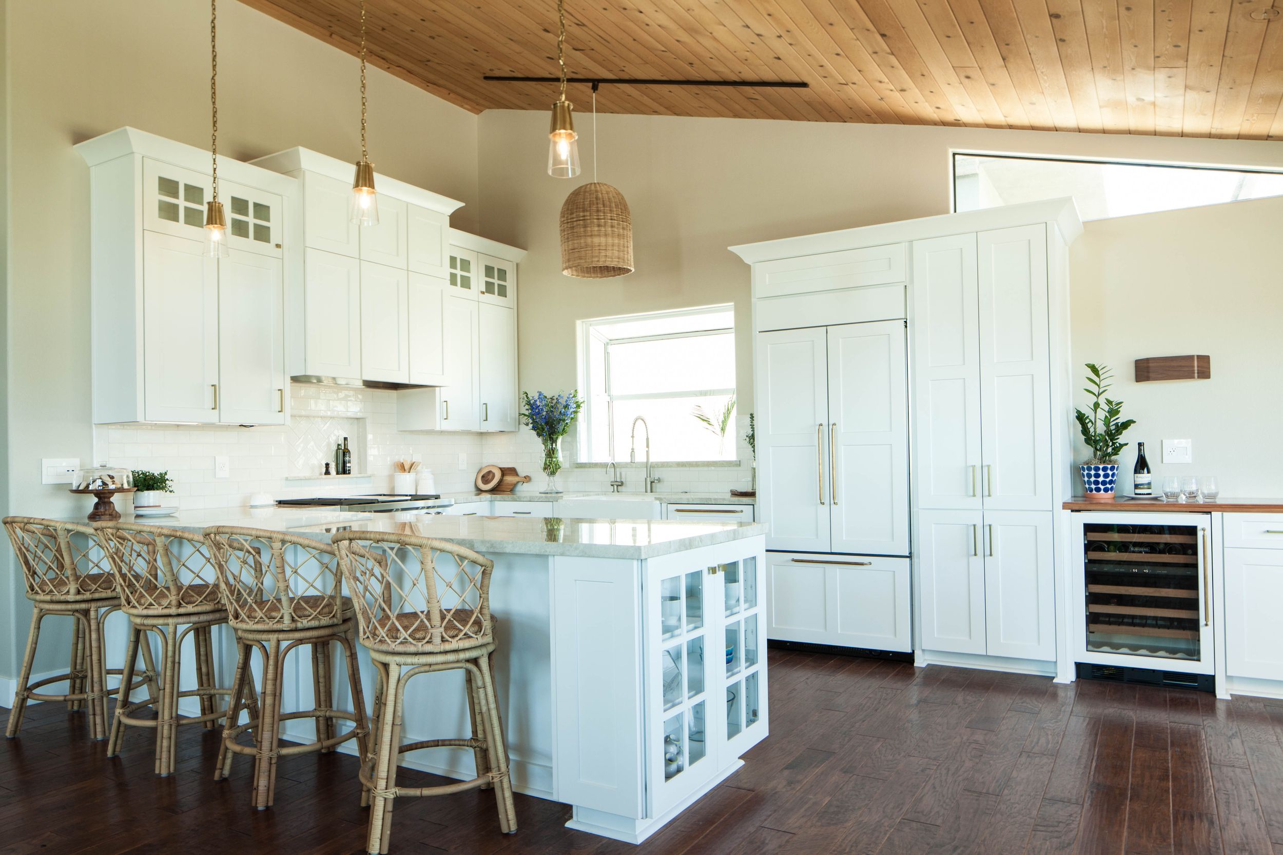 Modern farmhouse kitchen with white cabinets, wood ceiling, and bar seating around a central island.