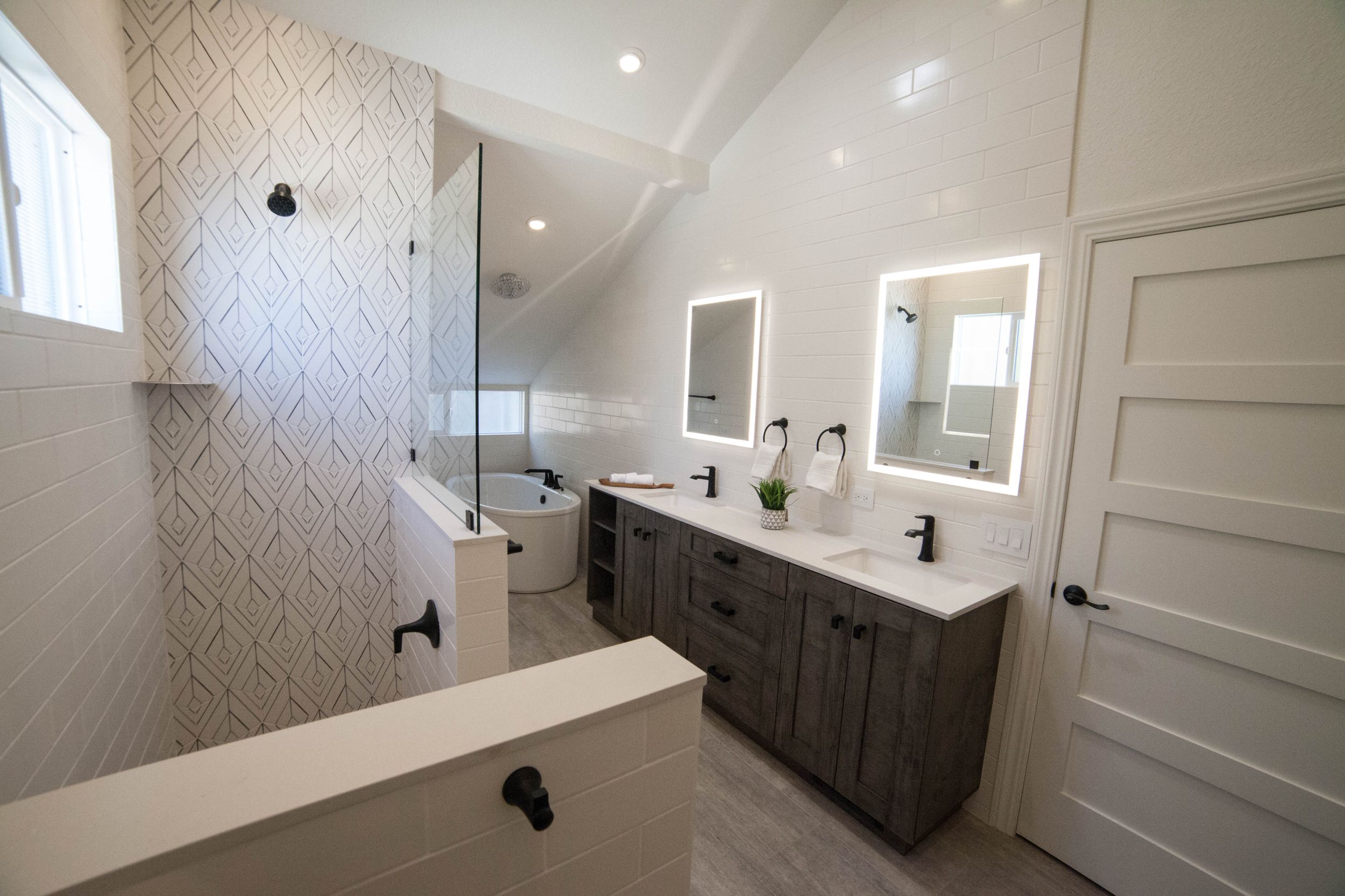 Contemporary bathroom featuring gray vanity, geometric wallpaper, and double sinks with modern fixtures.
