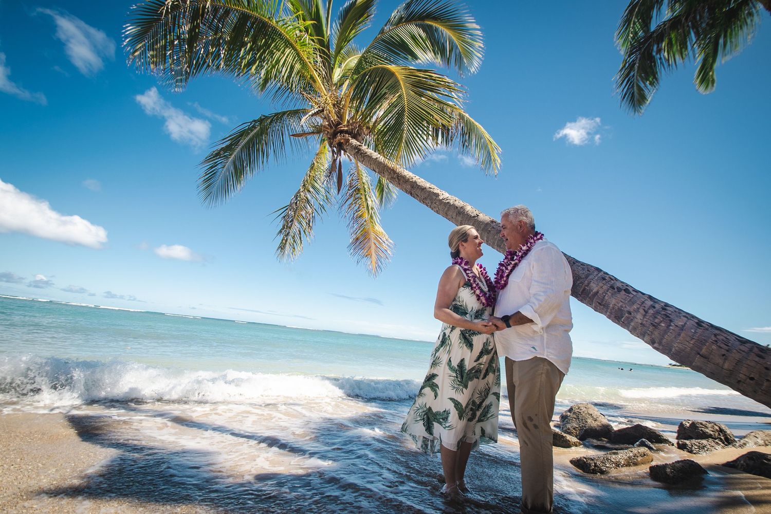 Couple embracing near a leaning palm tree on a tropical beach with turquoise waters.
