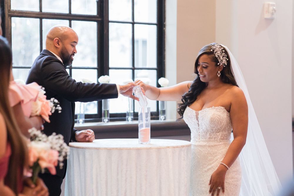 Couple participates in sand ceremony ritual at elegant indoor wedding venue.