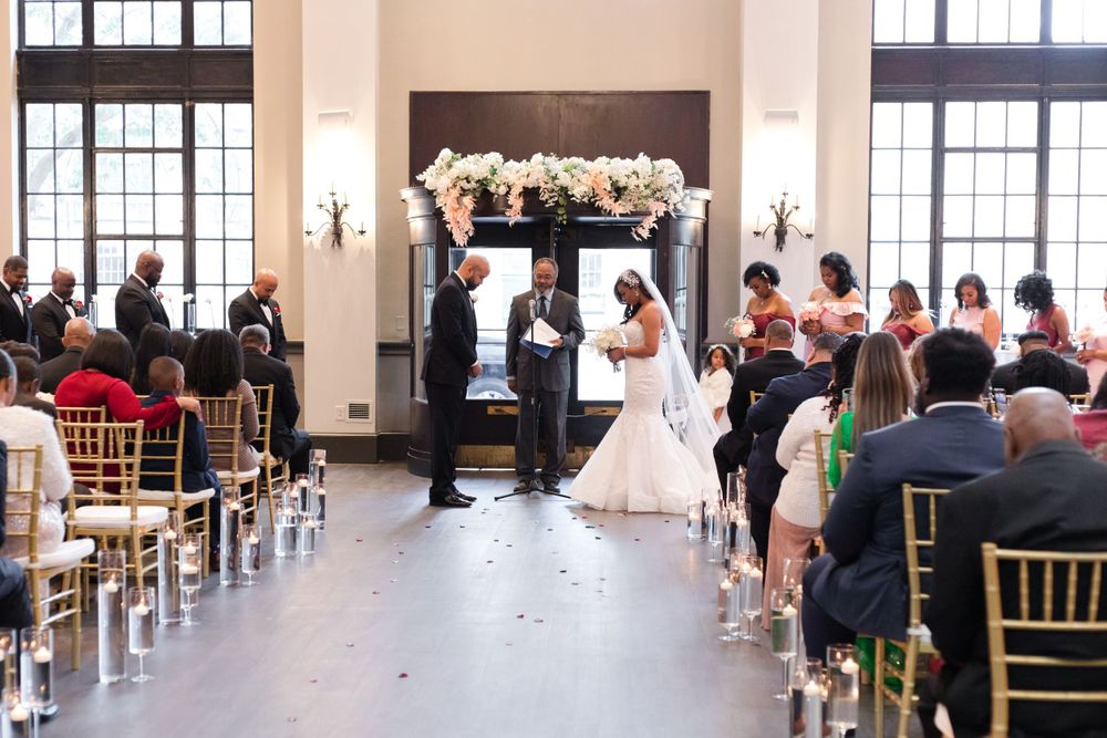 Indoor wedding ceremony with white floral arch and gold chiavari chairs in an elegant venue.