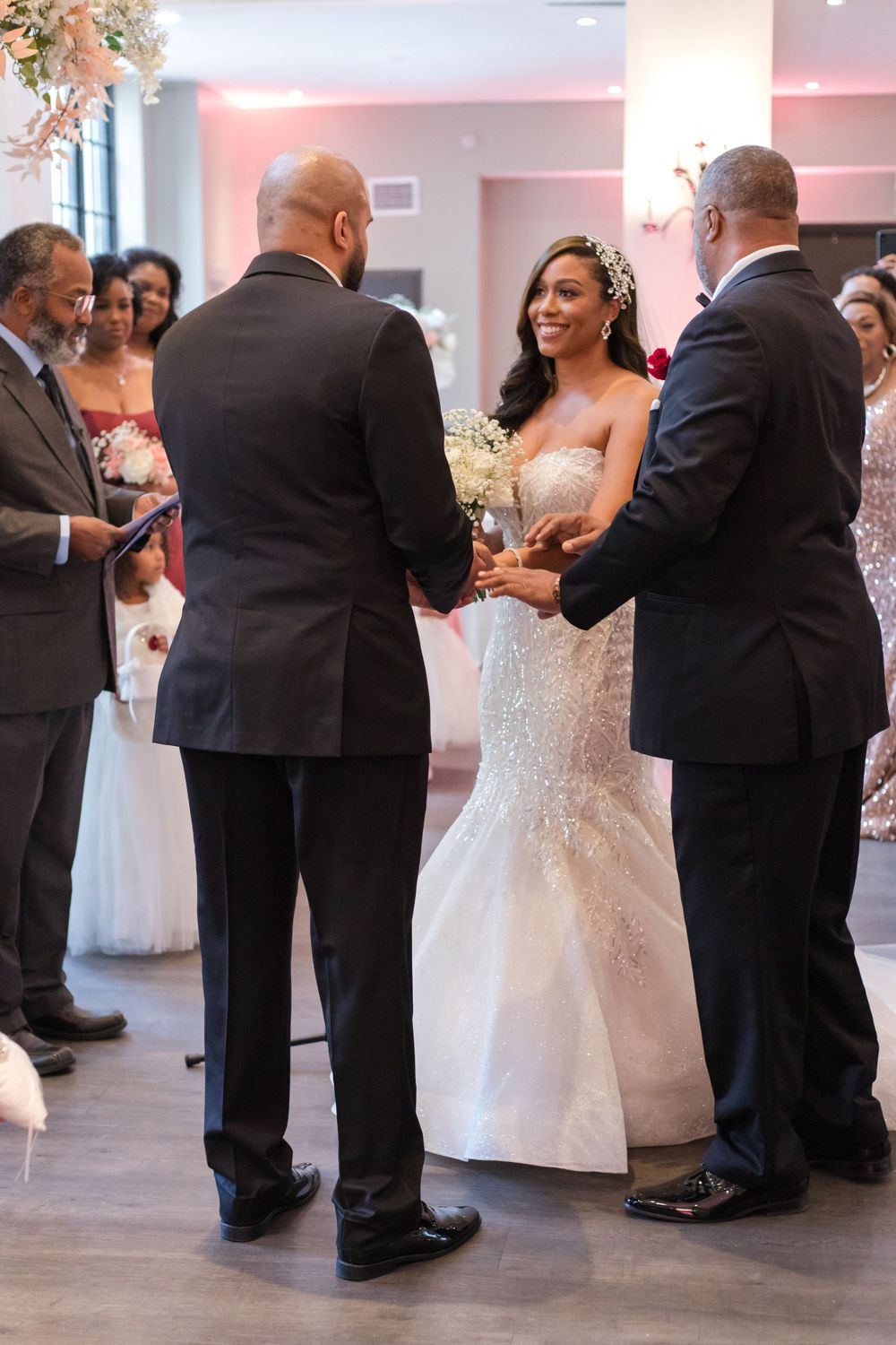 A wedding ceremony scene with attendees gathered around a bride in a white lace gown.