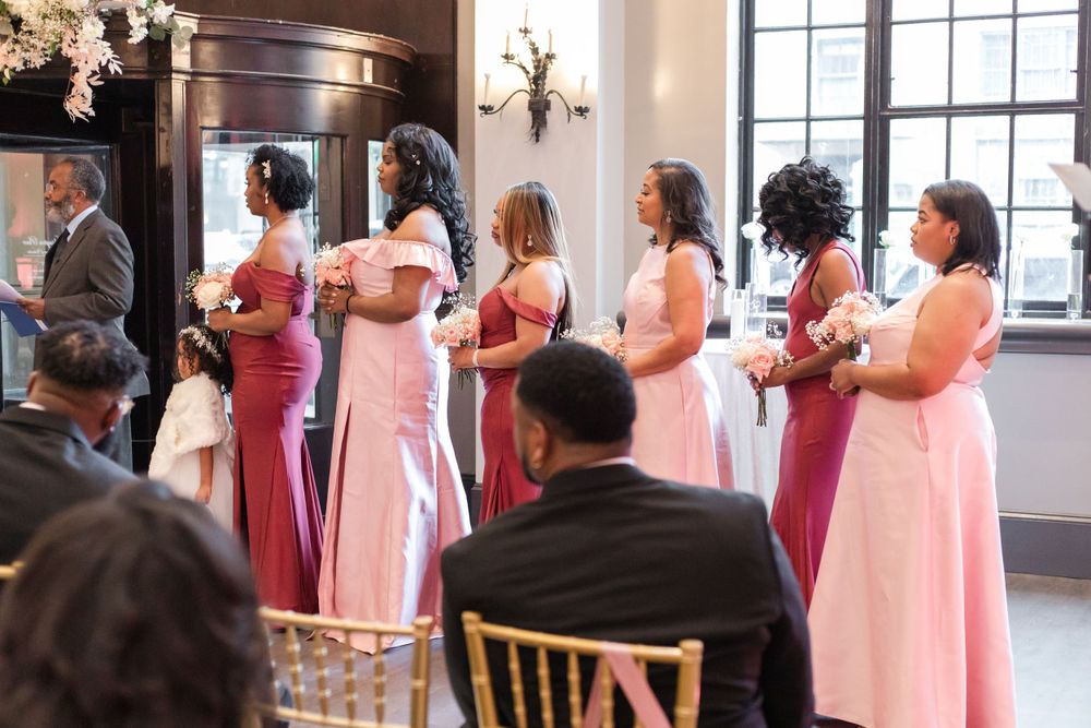 Wedding party members in pink gowns stand in formation during an indoor ceremony.