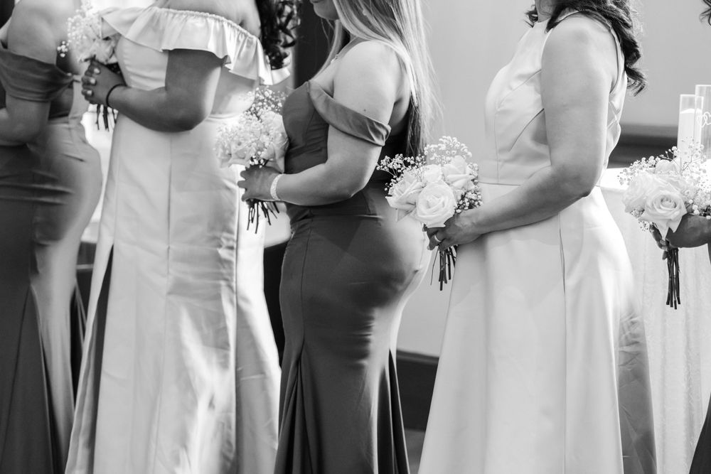 Bridesmaids in long elegant dresses hold bouquets while standing together in black and white.