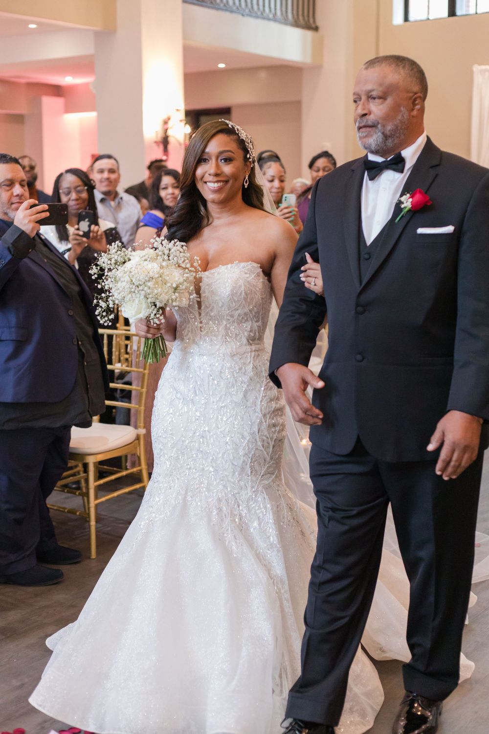 A wedding ceremony with guests seated in gold chairs watching as the couple walks down the aisle.