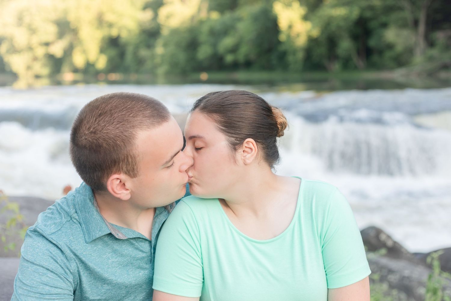 A romantic moment captured between two people by a flowing waterfall in soft lighting.