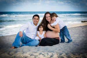Family photo session at the beach with casual poses on the sand at sunset.