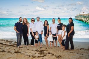 Family beach portrait session with group posed casually on sandy shore near ocean.