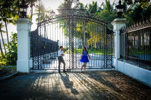 Silhouetted figures walking through ornate white gates in tropical garden setting.