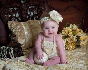 Baby photography on cream bedding with vintage pearls and lace accessories.