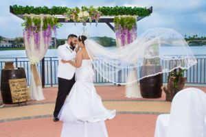 Wedding veil flowing dramatically in breeze during waterfront photo session.