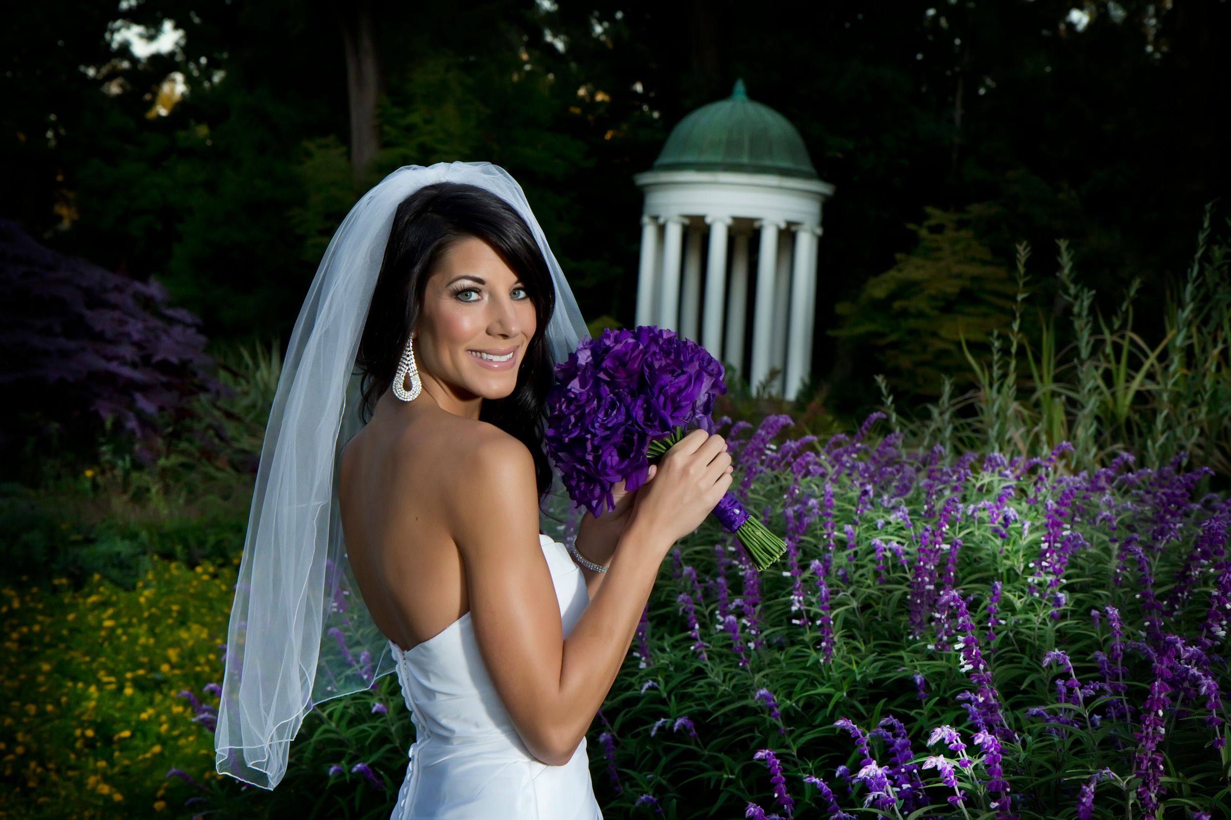 Artistic bridal portraits in a garden with purple delphinium flowers and evening lighting.