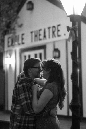 Black and white photo of a couple sharing a romantic moment outside the Empire Theatre at night.