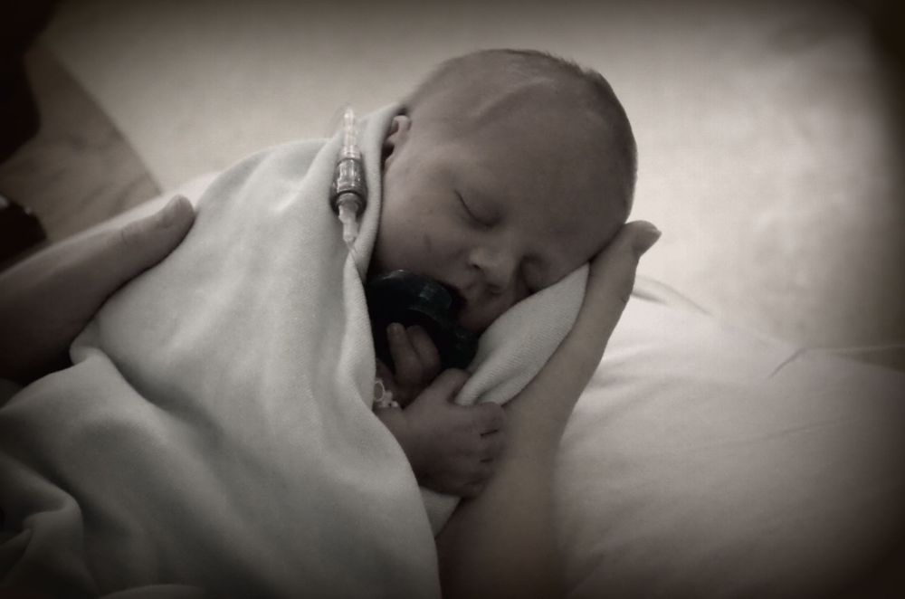 Black and white image of sleeping infant swaddled in white blanket.