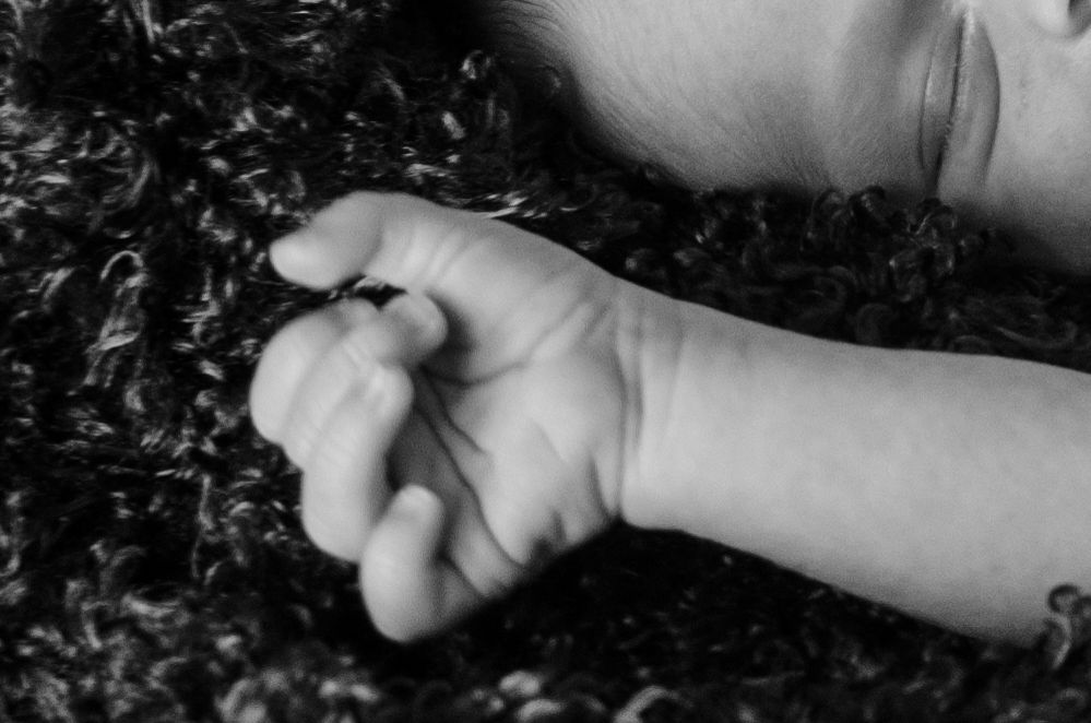 Close-up black and white photo of a tiny baby hand against a dark textured background.