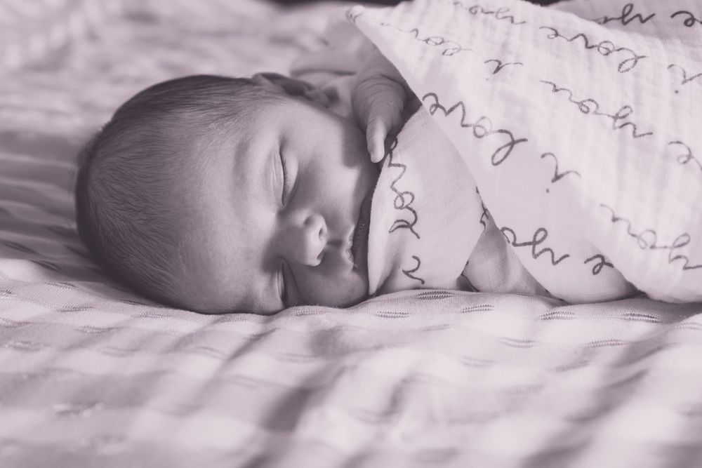A peaceful sleeping newborn wrapped in a patterned white swaddle.