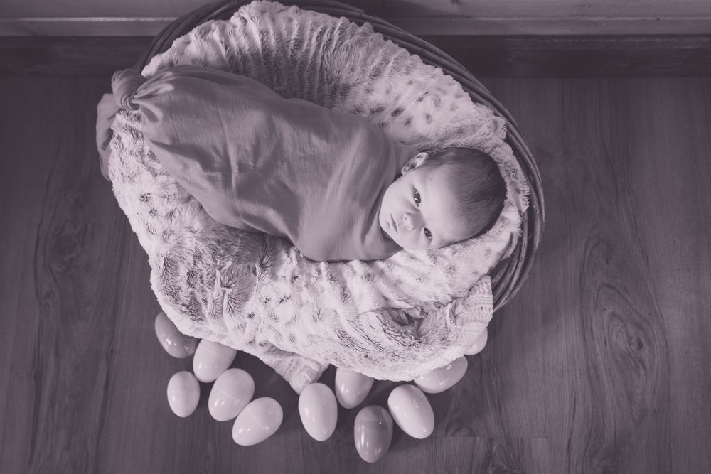 A newborn sleeping in a rustic round basket on wooden floor.