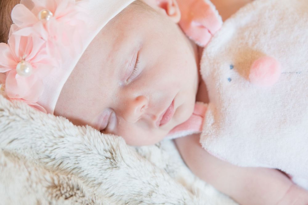 A sleeping baby wearing pink accessories rests on soft fur blanket.