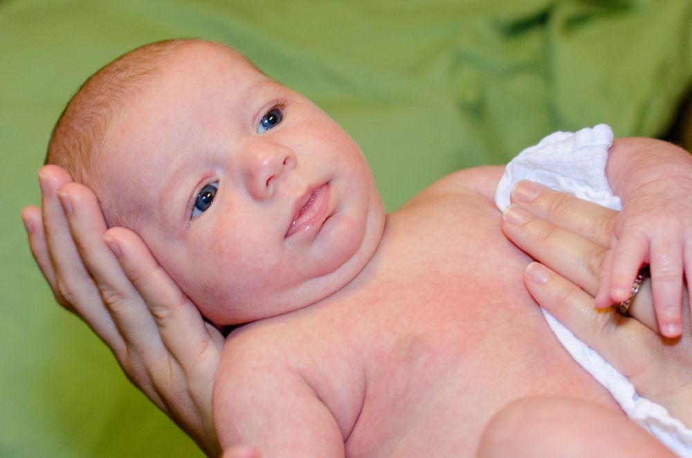 Infant lying on green surface with hands gently cradling their face.