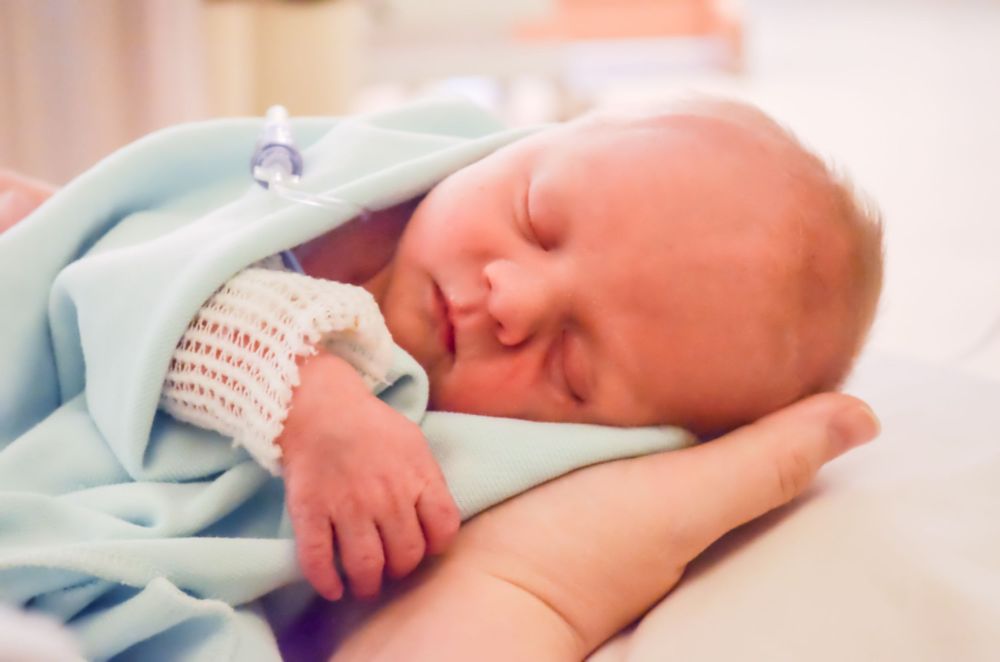 Peaceful sleeping infant wrapped in light blue blanket with hospital ID bracelet.