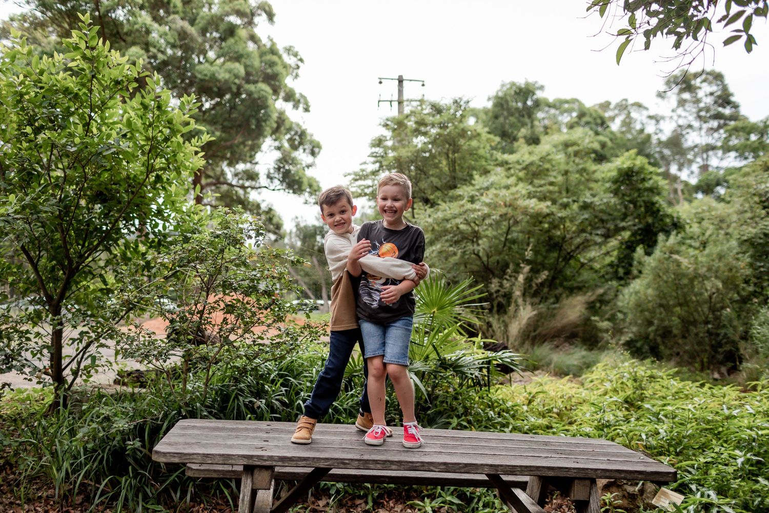Two people standing together on a wooden platform in a lush garden setting.
