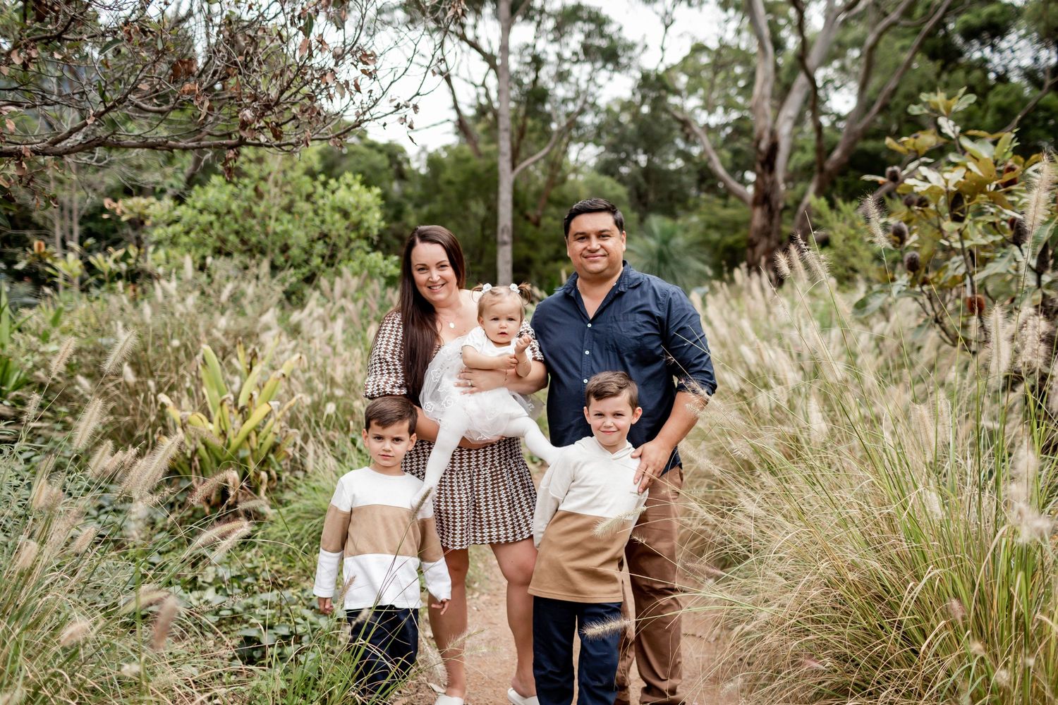 A family of five walking together on a nature trail surrounded by greenery.