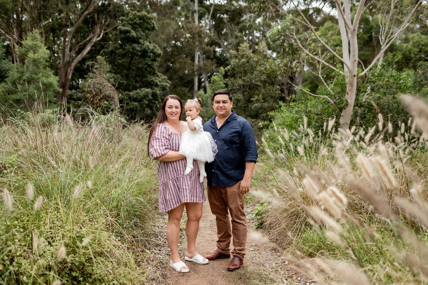 A trio poses for a photo on a scenic walking path surrounded by tall grass and trees.