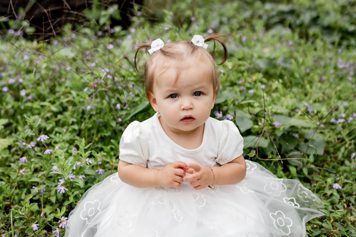 Small child in a white tulle dress poses in a garden setting.