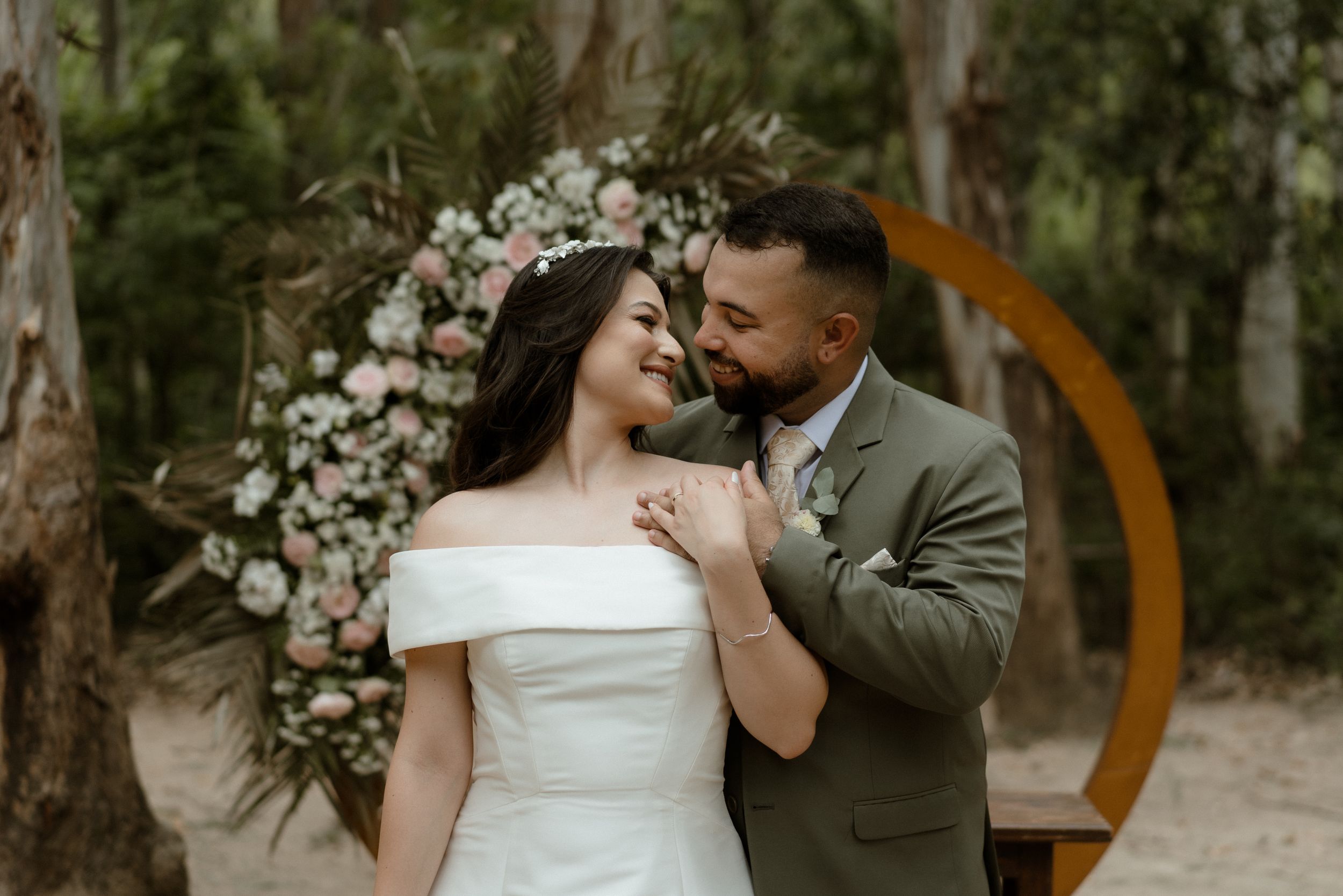 Wedding couple dancing together near wooden arch decorated with white flowers.