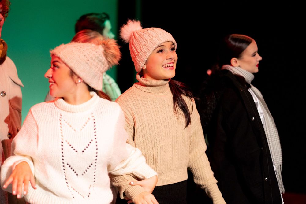 Three actors wearing winter jumpers and wooly hats looking around in wonder as part of a dramatic stage show