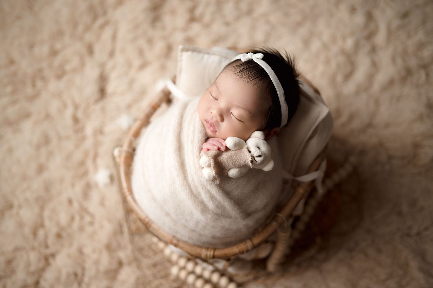 Aerial shot of sleeping newborn in white wrap on textured beige background.