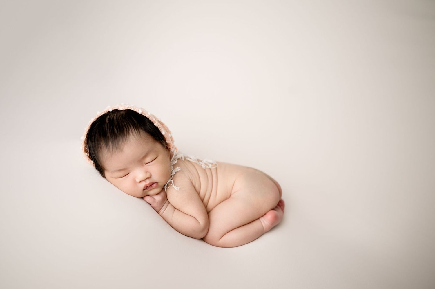 Artistic newborn photography with sleeping baby on minimal white background.