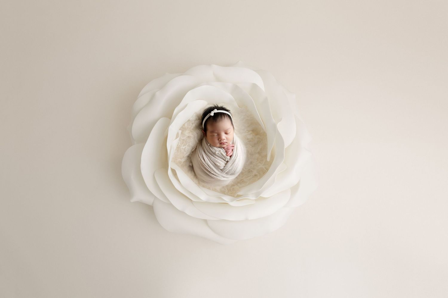 Newborn wrapped in white fabric nestled in large white fabric flower prop.