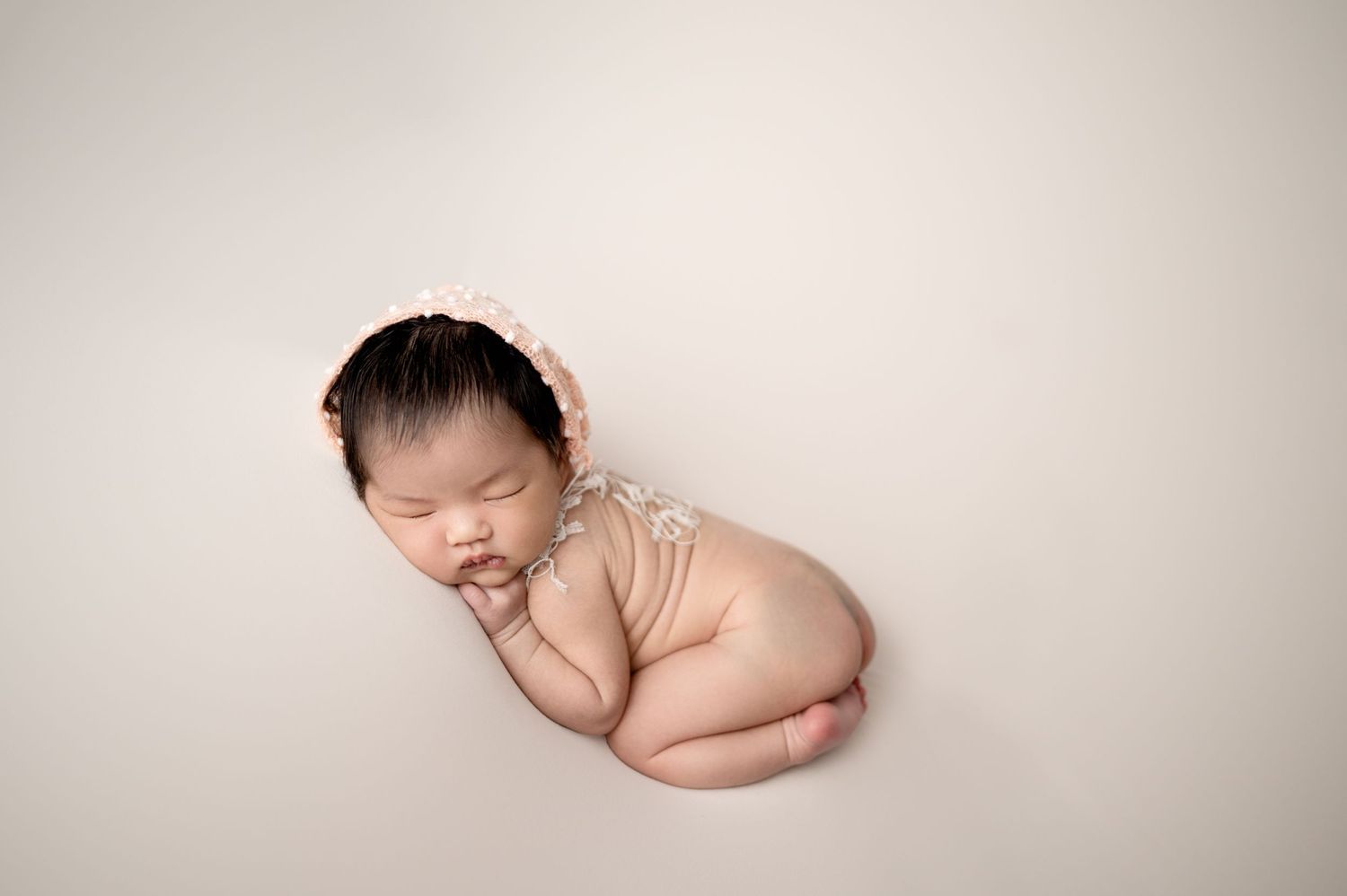 Peaceful newborn baby sleeping in curled position on beige background.