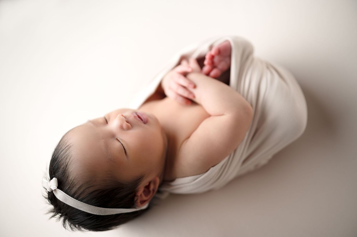 Artistic overhead shot of newborn in white wrap against light background.