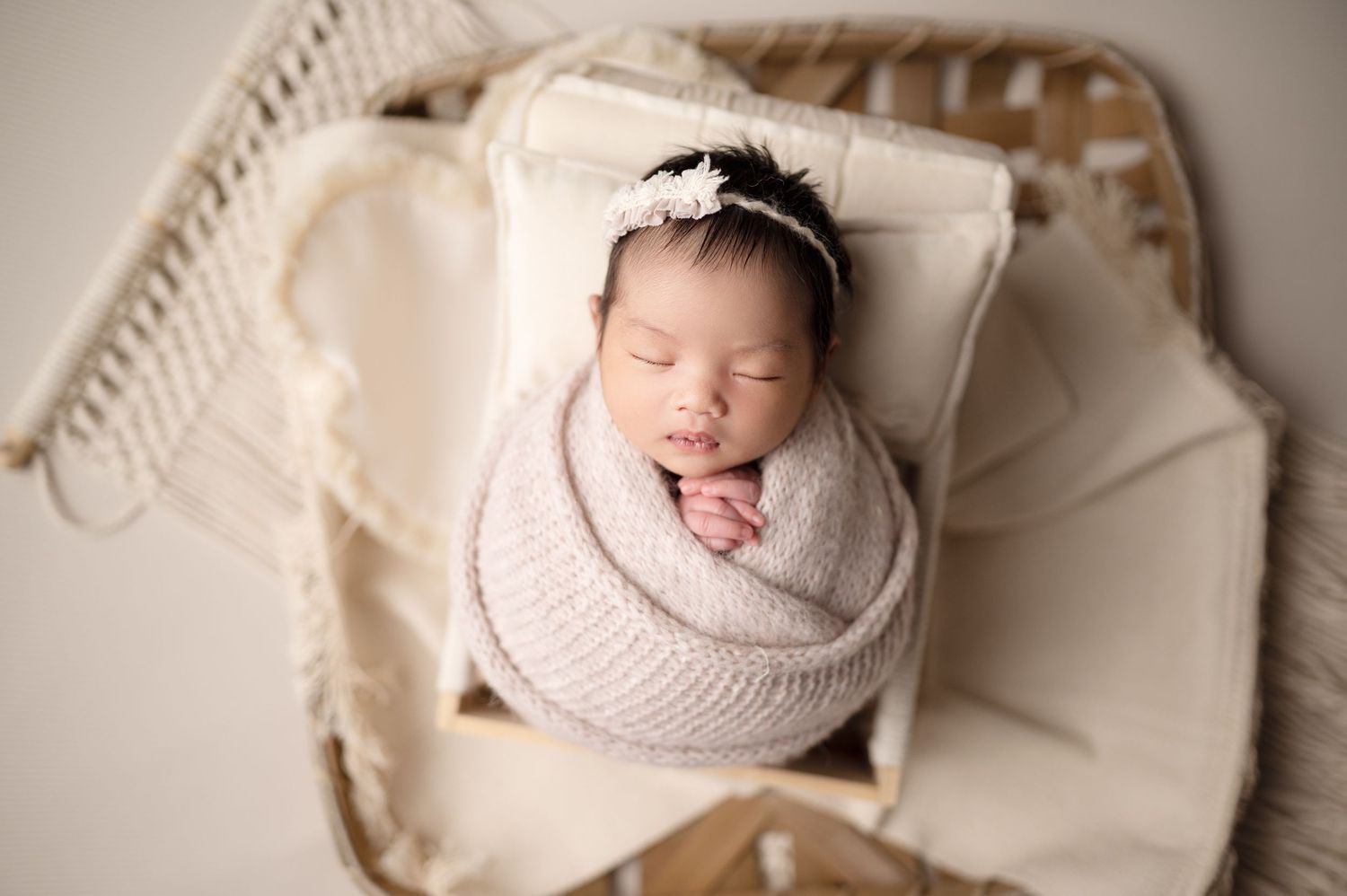 Sleeping newborn wrapped in knit swaddle on vintage white cushioned chair.