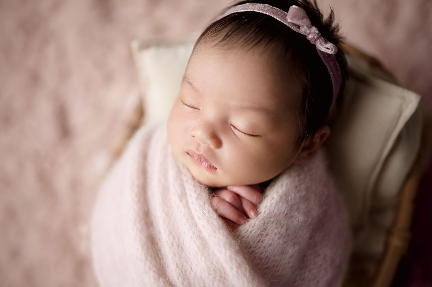 Professional portrait of sleeping newborn in pink wrap with delicate headband.