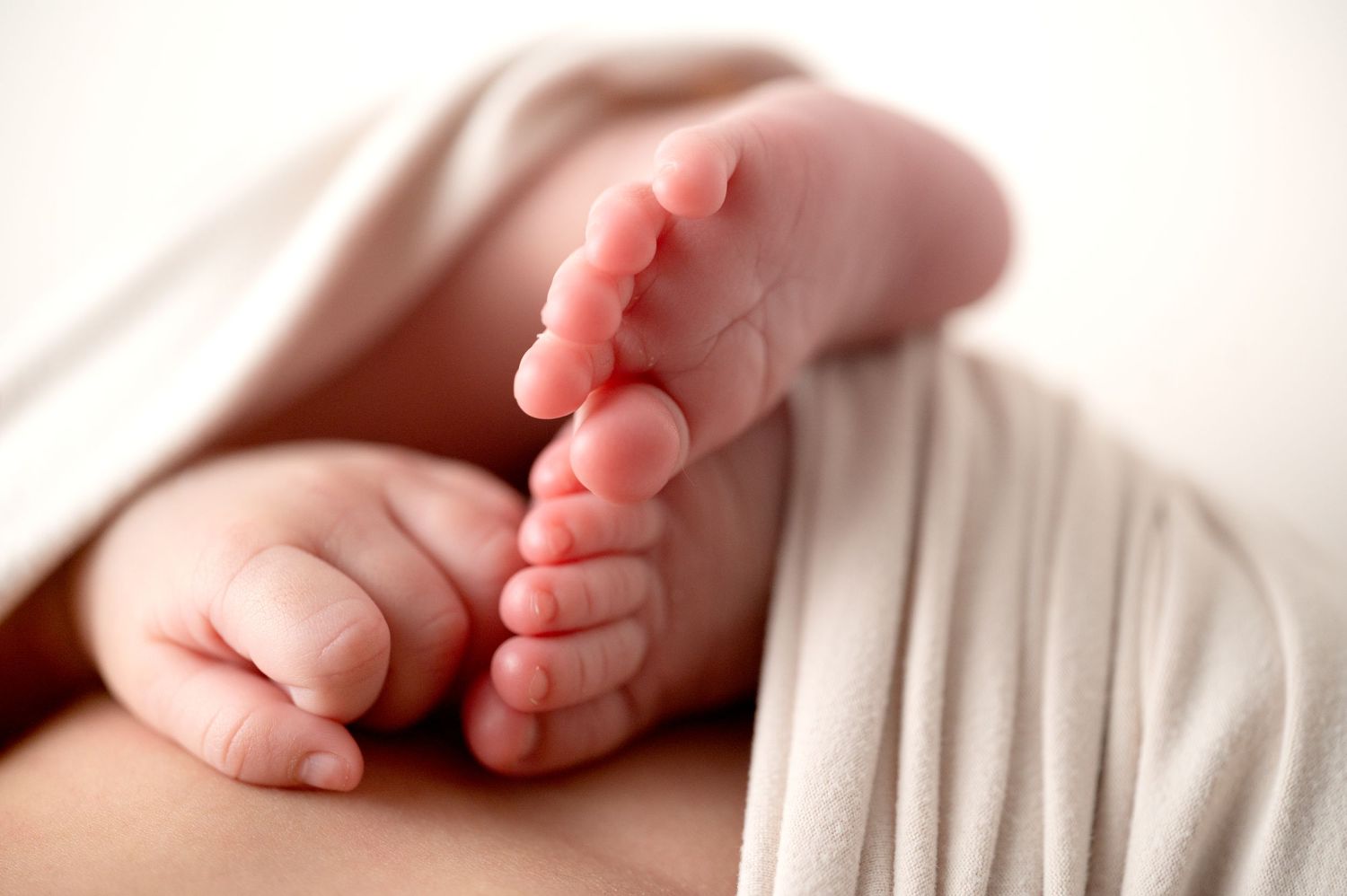 Close-up of tiny newborn baby feet and toes against white fabric.