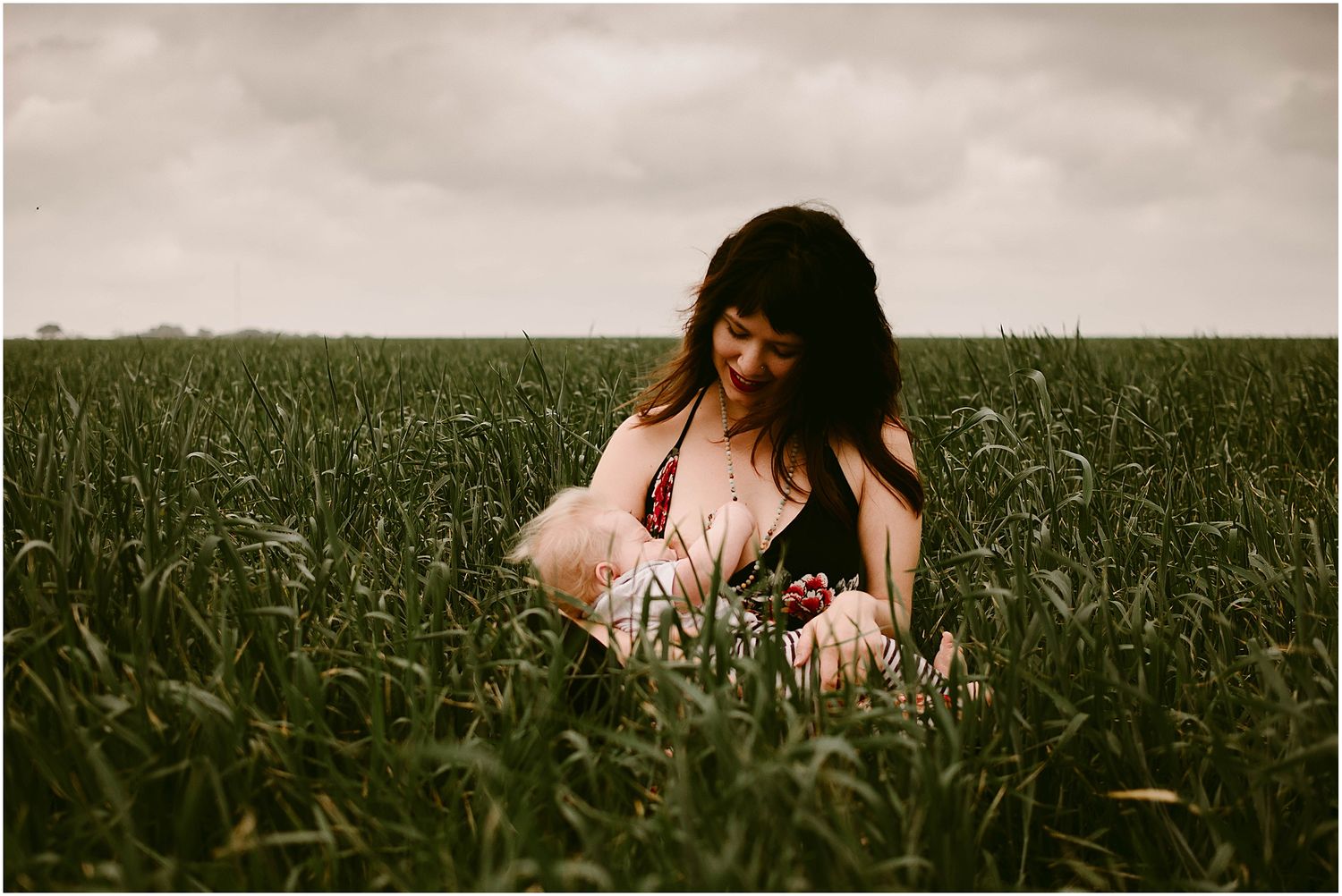 Intimate nursing portrait captured in wild grass field at dusk.