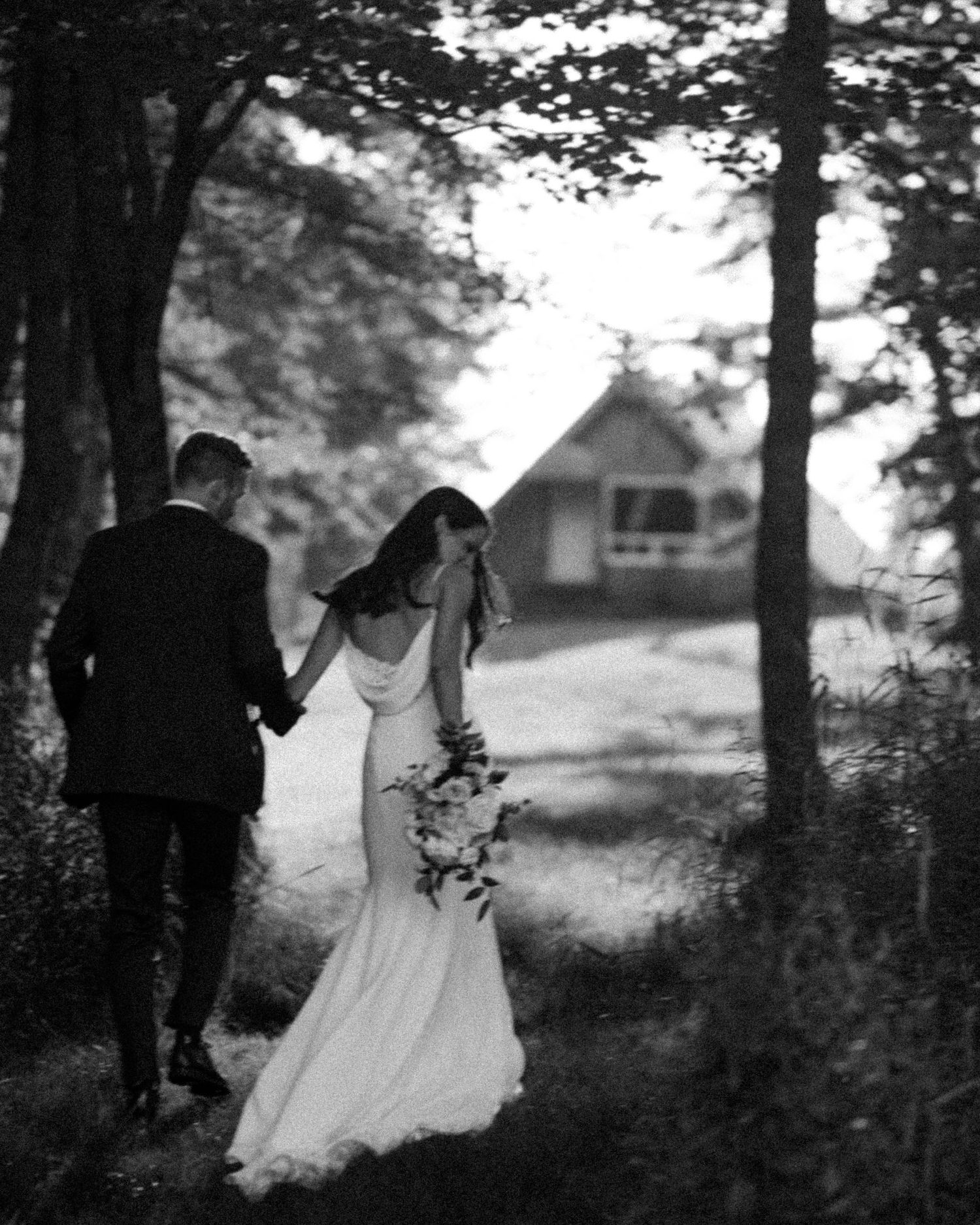 A black and white wedding photo captured in a wooded setting with dramatic lighting.