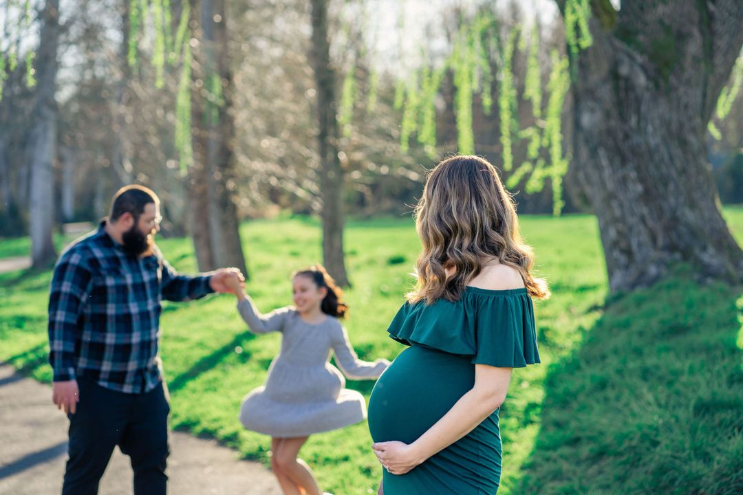 portrait of pregnant mama with dad and daughter playing in the background