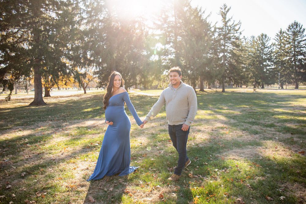 Couple walking hand in hand during sunset maternity photo session in wooded park.