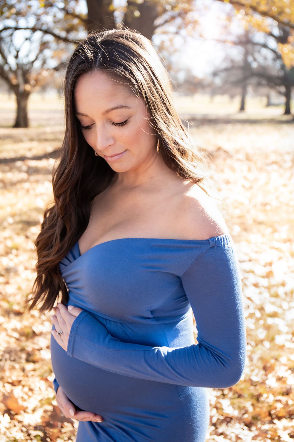 Expectant mother in blue off-shoulder dress poses during autumn outdoor photo session.