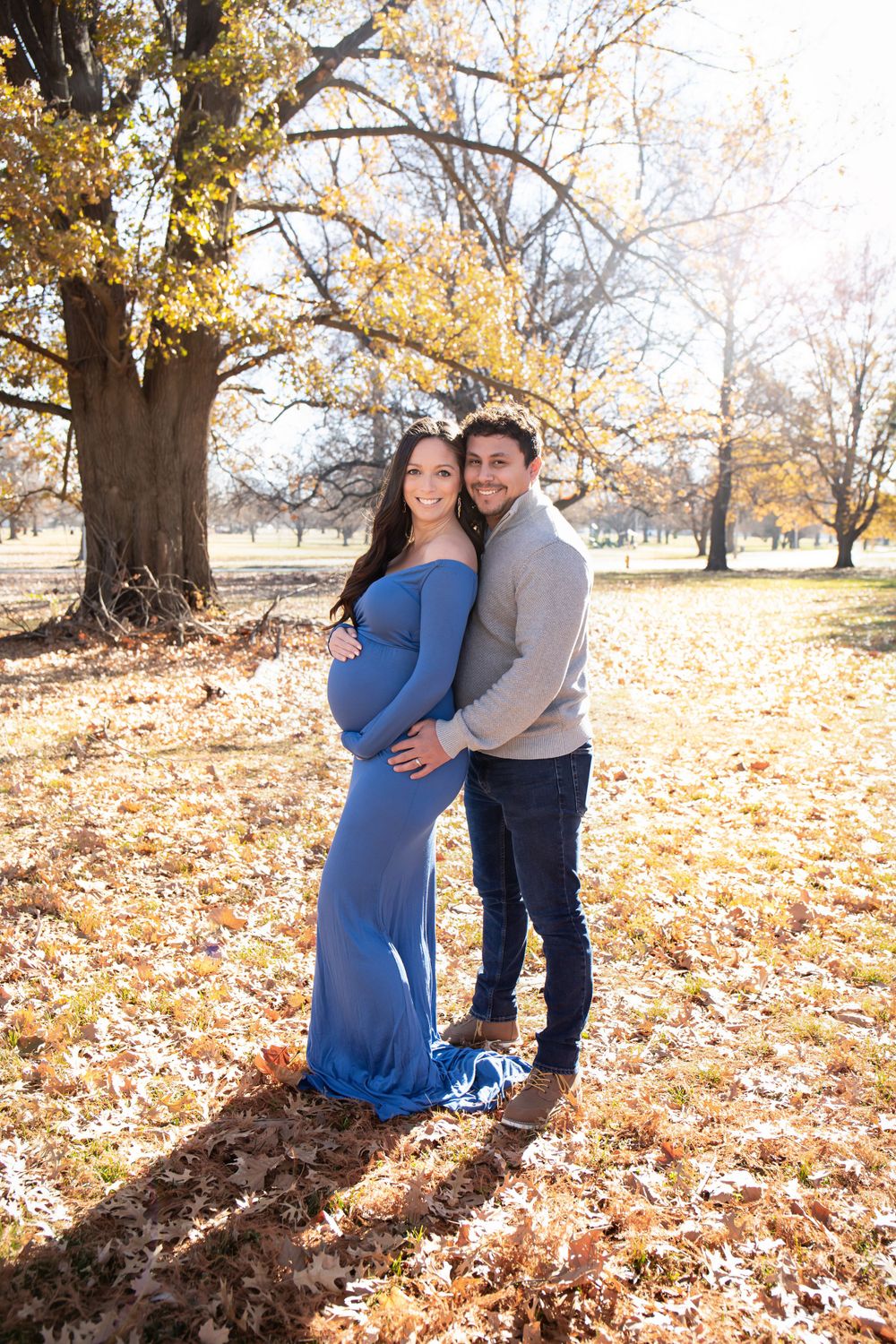 A maternity photo shoot in a park with fall foliage and golden afternoon light.